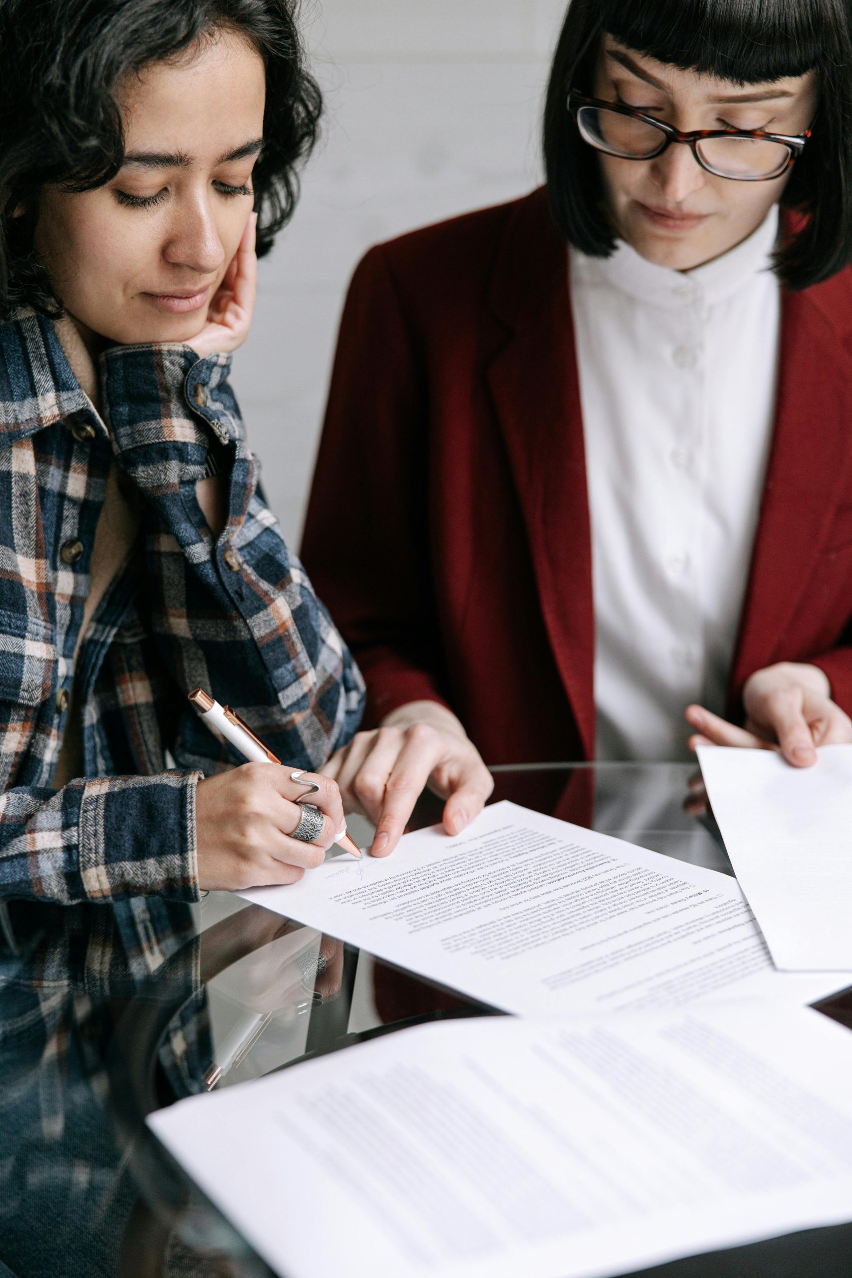 Two adult women reviewing and signing paperwork together at a table during a home sale discussion