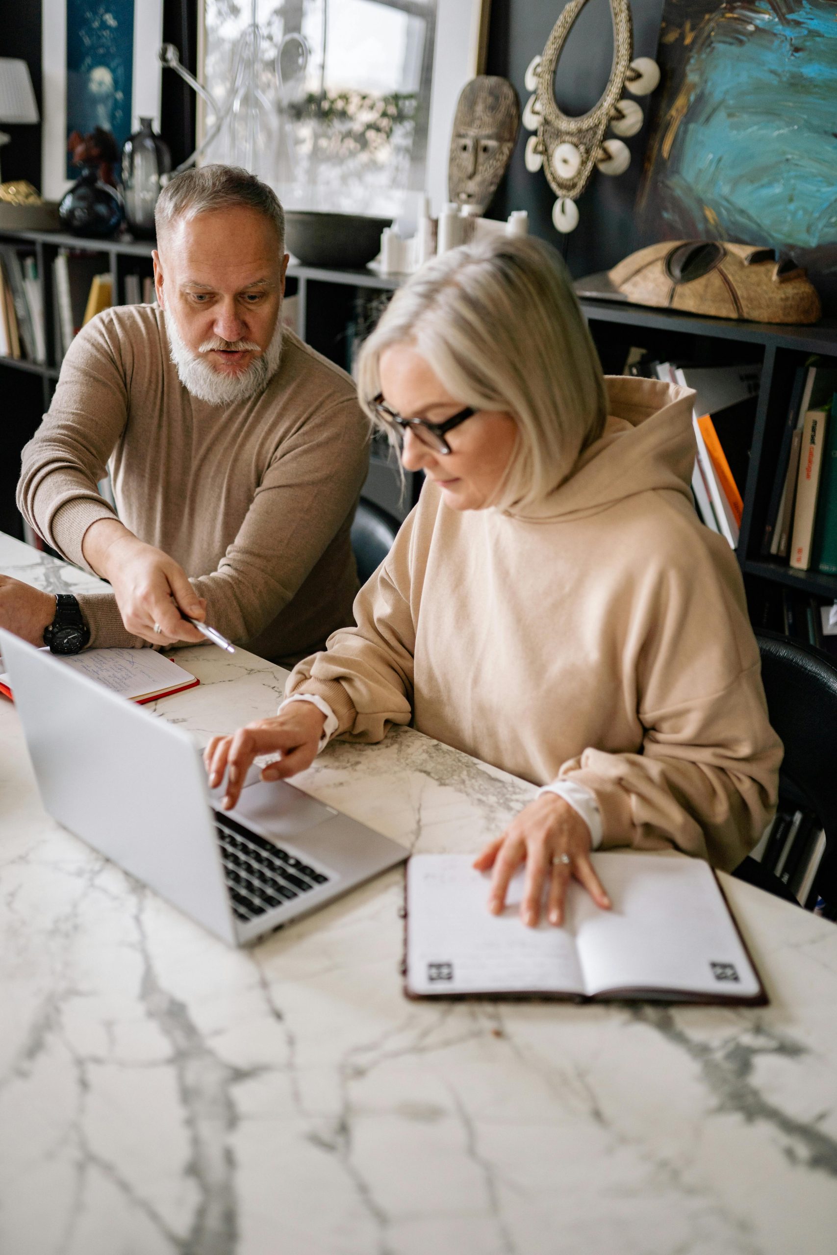 Older couple reviewing financial documents together at a kitchen table while using a laptop