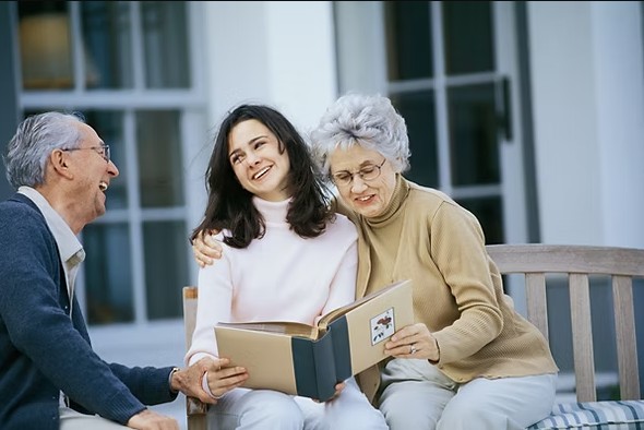 Adult daughter sitting with her aging parents on a bench, looking through a photo album together