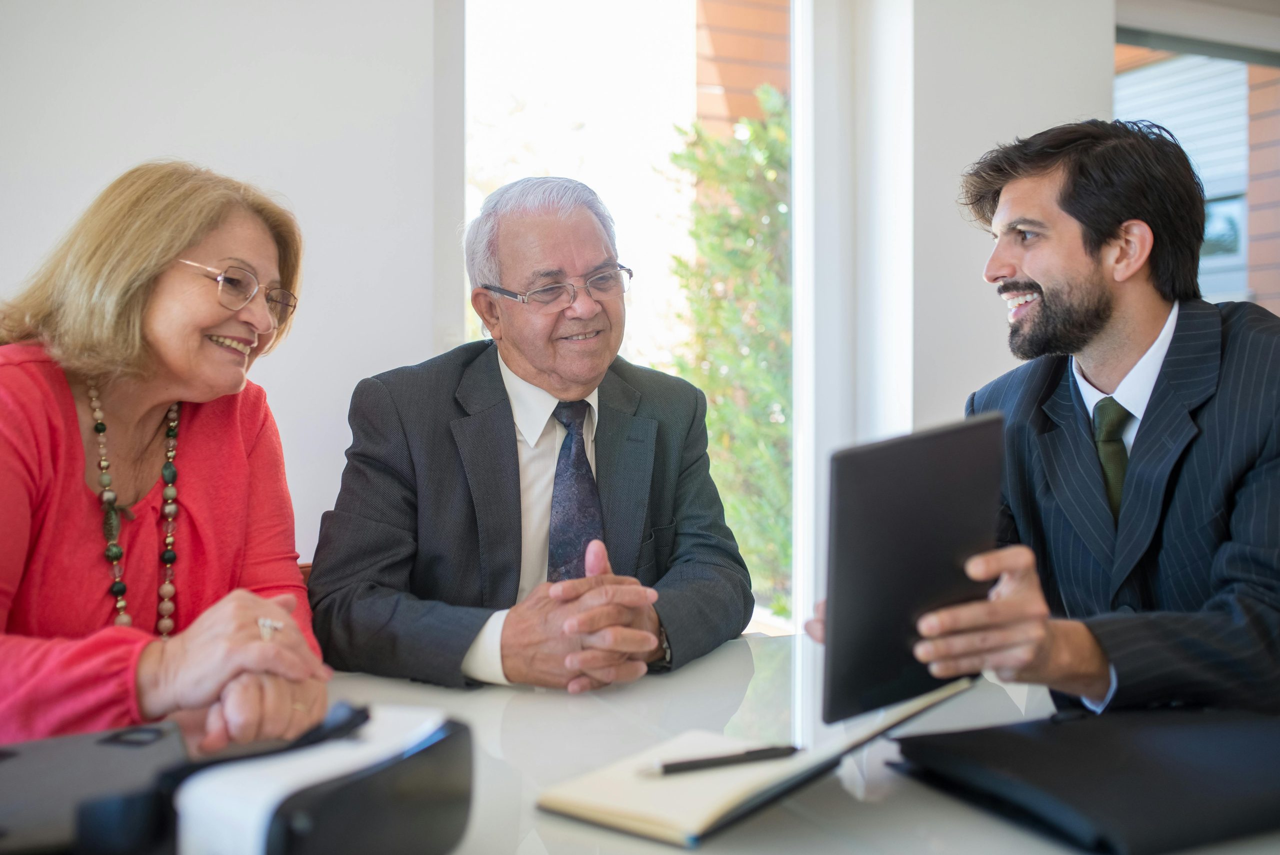 Older couple meeting with a financial advisor at a table reviewing information on a tablet.