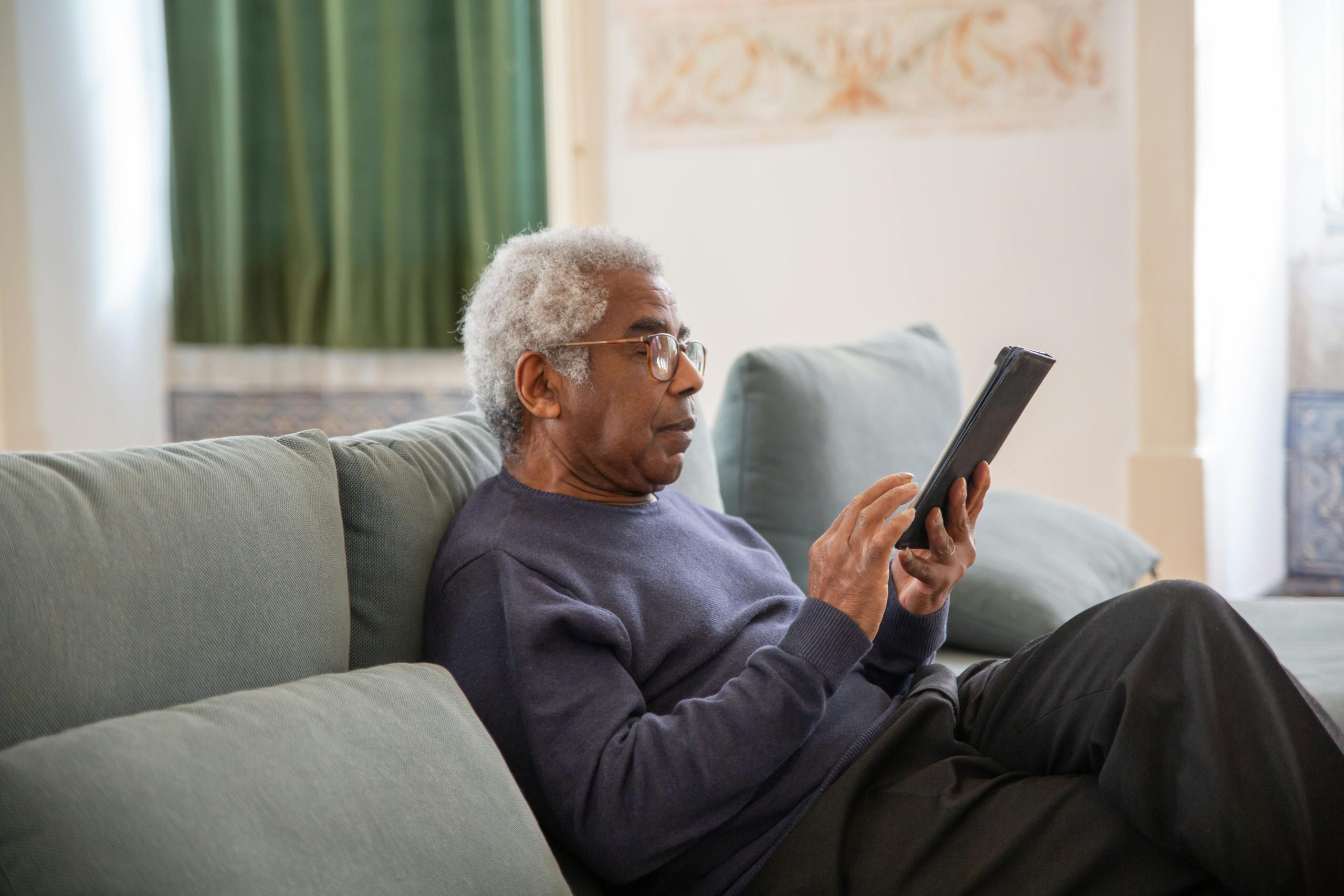 Older man sitting on a sofa at home using a tablet device