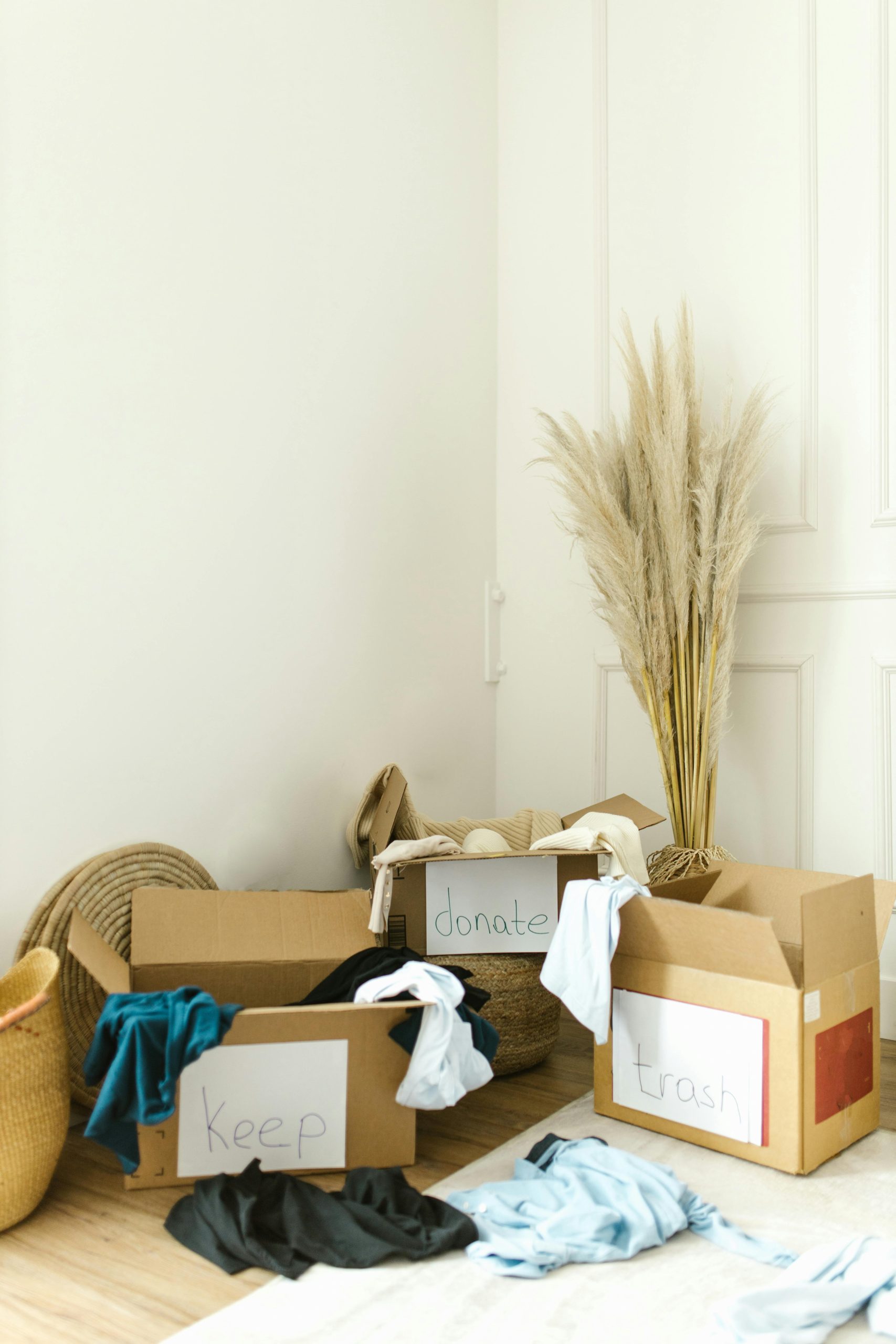 Cardboard boxes labeled “Keep,” “Donate,” and “Trash” in a bright room with clothing sorted for a move.